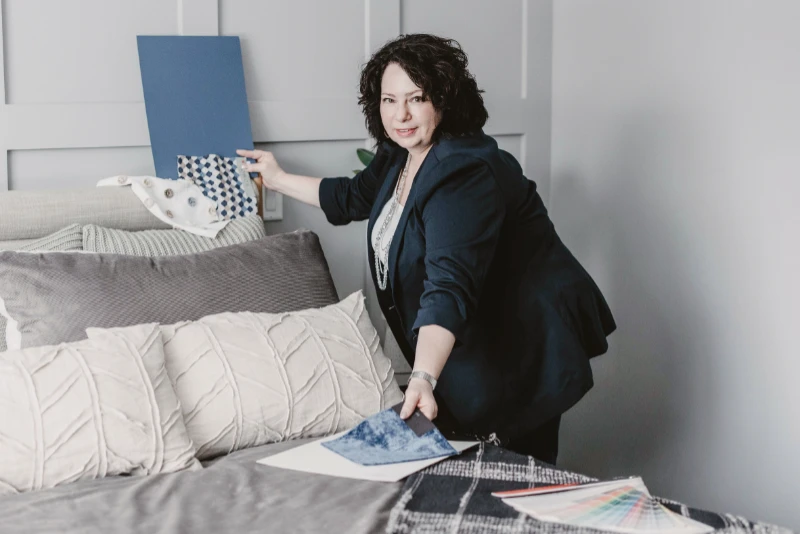 Interior designer holds blue colour and fabric swatches up to a panelled wall in a bedroom.