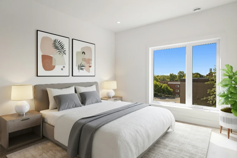A bright, clean bedroom, with white and grey linens on the bed, double nightstands each with a small white lamp, and a healthy plant sits next to the wide windows with blue skies outside.