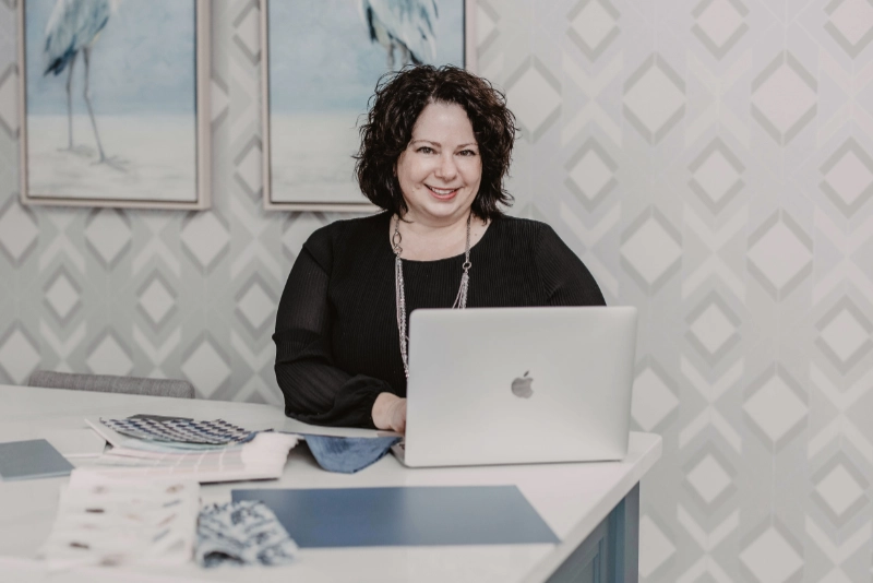 Interior designer, Trina MacPhee, sits with her laptop open. Decorating fabrics and colour swatches sit on the table.