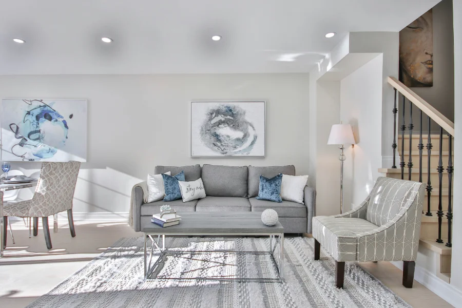 A bright basement sitting room with a grey couch and blue and white cushions, similar colours adorn accents and paintings on the walls
