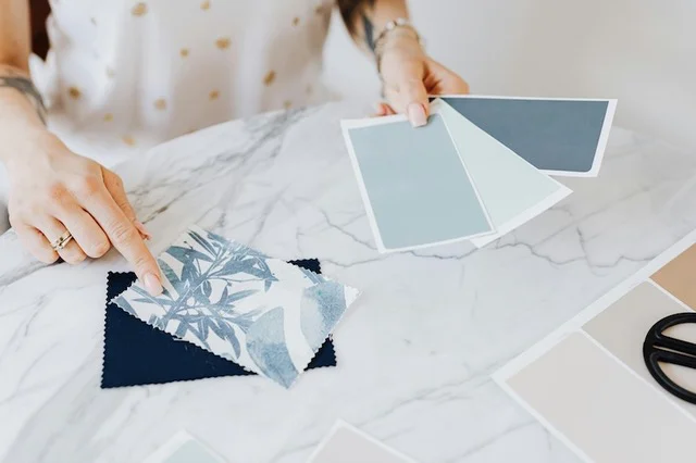 An interior designer reviews several varied blue color swatches while pointing to a patterned fabric swatch on a table.