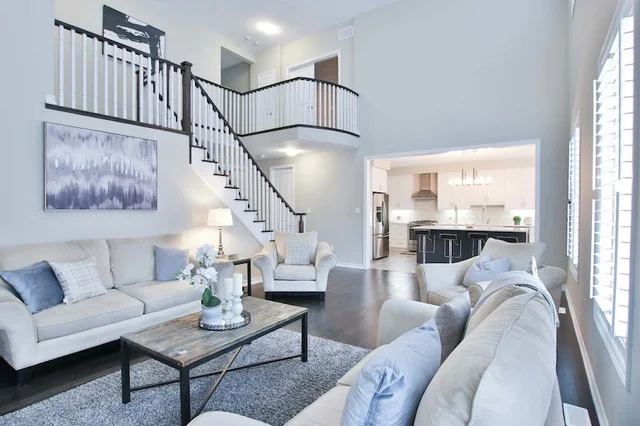 A bright, white livingroom with light blue accents, and a stairwell leading to a second floor landing.